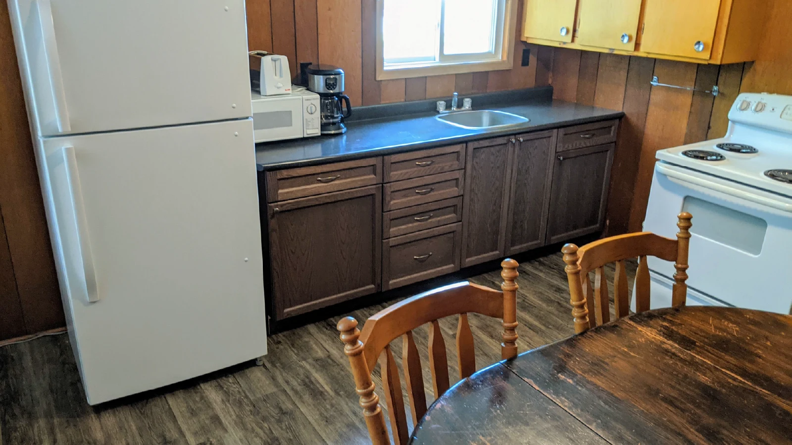 Pigeon Lake Resort Cottage nineteen kitchen with refrigerator, stove, sink, microwave, coffee maker, and wooden cabinets.